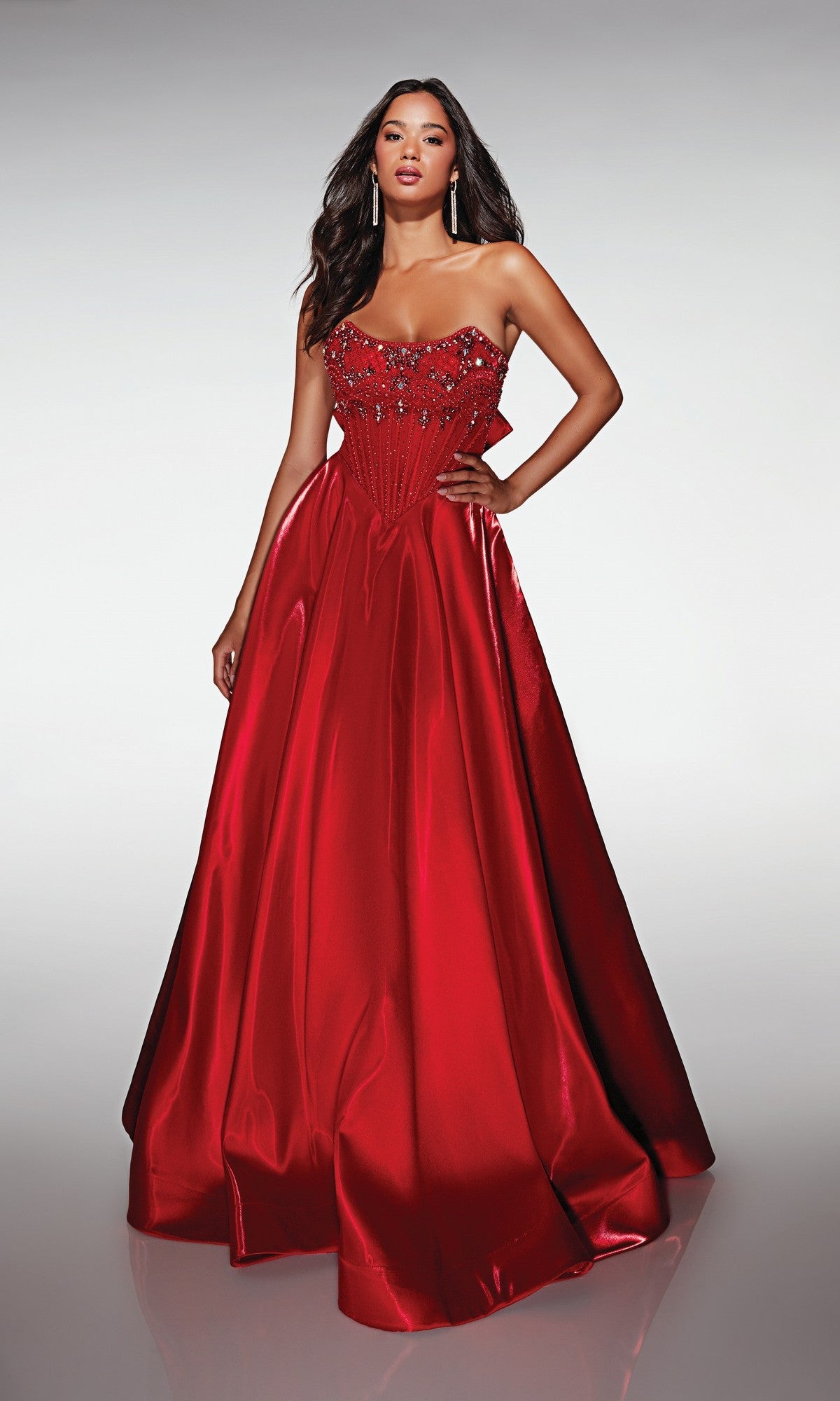 A woman models the Alyce 62134 Long Prom Dress, a floor-length strapless red satin ball gown with beaded bodice, standing elegantly against a plain light gray background.